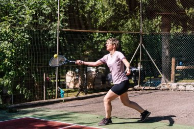 Tenis oynayan bayan sporcu, parlak güneş ışığı altında parlak bir yaz gününde ustalıkla topa vuruyor.