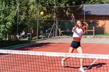Yoğunlaşmış kadın sporcu, kırmızı kil bir sahada gündüz tenis maçında güçlü bir forehand vuruşu yapıyor.