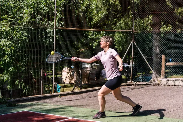 Tenis oynayan bayan sporcu, parlak güneş ışığı altında parlak bir yaz gününde ustalıkla topa vuruyor.