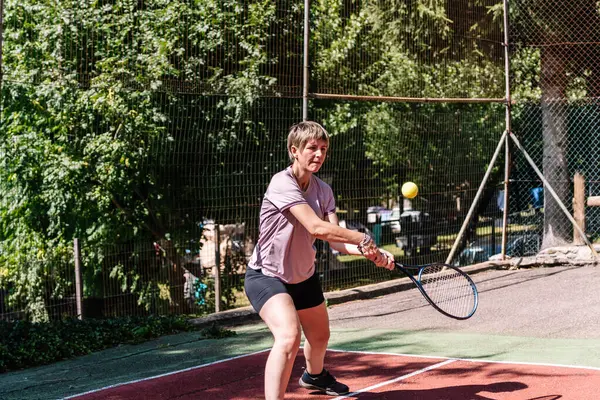Tenis oynayan konsantre sporcu kadın, güneşli bir günde kırmızı kortta raketle topa vuruyor.