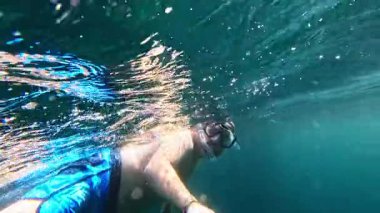 Snorkeler kristal berrak turkuaz suların tadını çıkarıyor, canlı deniz ortamı ile tropikal sualtı macerası sırasında coşkulu başparmaklar çakıyor.
