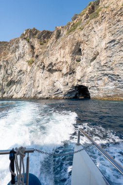 Beyaz tekne, güneşli bir yaz gününde, güllerin kayalık kıyılarında dalgalar ve köpükler yaratıyor.