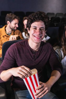 Sıcak bir sinemada arkadaşlarla film izlerken patlamış mısırın tadını çıkaran mutlu genç adam kahkahalarını paylaşıyor ve neşeli anılar yaratıyor.