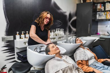 Kuaför müşterinin saçını yıkama, profesyonel şımartma ve modern güzellik salonu ortamında rahatlatıcı şampuan tedavisi.