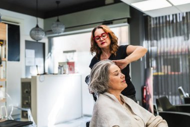 Modern bir güzellik salonunda profesyonel kuaför saç kurutma ve saç şekillendirme. Müşteri saç tedavisi sırasında dinleniyor.