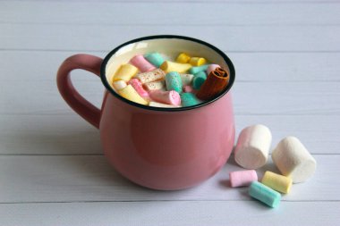 Çok renkli şekerlemeli sıcak çikolata ve gri arka planda pembe bardakta tarçın. 