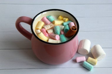 Çok renkli şekerlemeli sıcak çikolata ve gri arka planda pembe bardakta tarçın. 