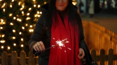 Kırmızı eşarplı genç bir kadın Noel ağacının yanında maytap yakıyor. Noel kenti kutlamaları 