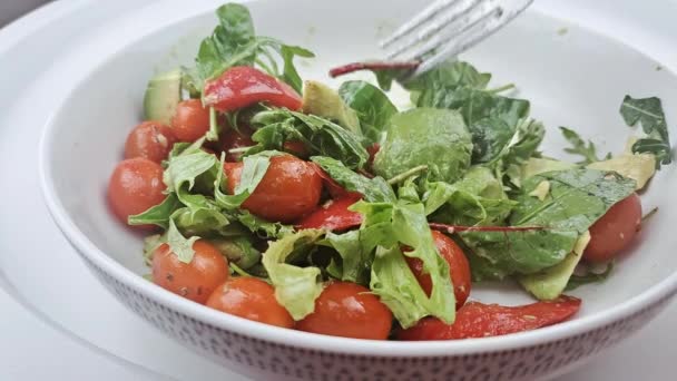 一盘新鲜的绿色沙拉 白菜叶 西红柿 黄瓜和鳄梨放在白桌上 — 图库视频影像