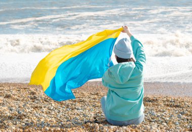 Ukrayna bayrağı taşıyan mavi kapüşonlu ve mavi şapkalı esmer kadın, vatanseverlik kavramı.