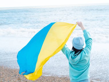 Ukrayna bayrağı taşıyan mavi kapüşonlu ve mavi şapkalı esmer kadın, vatanseverlik kavramı.