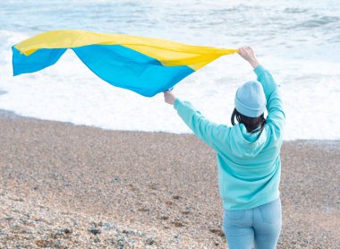 Ukrayna bayrağı taşıyan mavi kapüşonlu ve mavi şapkalı esmer kadın, vatanseverlik kavramı.