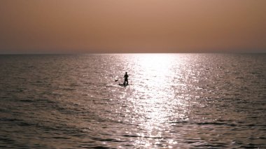 silhouette of person doing sup surfing on the sunset in the blue sea. clipart