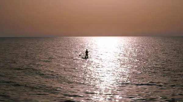 Stock image silhouette of person doing sup surfing on the sunset in the blue sea.