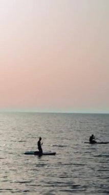 Sörfçüler günbatımında sörf tahtasında yüzerler..