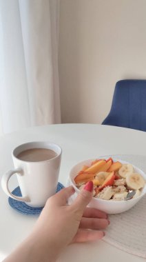 Bir kase yulaf ezmesi ve sabah beyaz masada sütlü kahve, vejetaryen kahvaltısı.