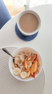 Bir kase yulaf ezmesi ve sabah beyaz masada sütlü kahve, vejetaryen kahvaltısı.