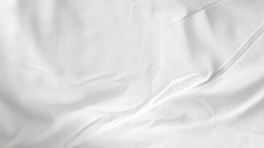 Kırışık battaniyeli beyaz çarşaflar sade arka planda, modern yatak odası düzeninde..