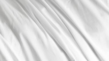 Kırışık battaniyeli beyaz çarşaflar sade arka planda, modern yatak odası düzeninde..