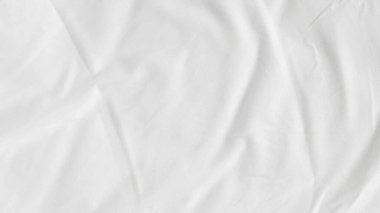 Kırışık battaniyeli beyaz çarşaflar sade arka planda, modern yatak odası düzeninde..
