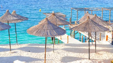 Sahilde güneşin altında saman plaj şemsiyeleri kumlu sahilde gölge yaratıyor..