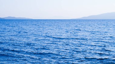 Güneşli gökyüzünün altında berrak mavi sakin deniz, doğal güzellik ve sükuneti yansıtıyor.
