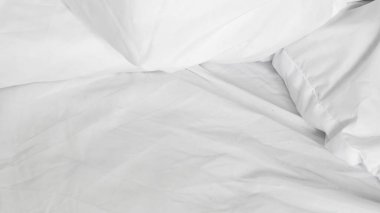 Yapılmamış beyaz bir yatak ve doğal sabah ışığı olan minimalist bir iç mekan.