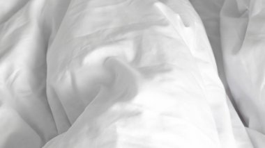 Yapılmamış beyaz bir yatak ve doğal sabah ışığı olan minimalist bir iç mekan.