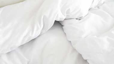 Beyaz yorgan ve yastık rahat bir yatakta otel sakinliğini ve spa ortamını gösteriyor..