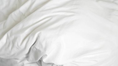 Beyaz yorgan ve yastık rahat bir yatakta otel sakinliğini ve spa ortamını gösteriyor..