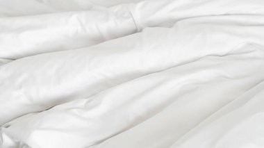 Beyaz yorgan ve yastık rahat bir yatakta otel sakinliğini ve spa ortamını gösteriyor..