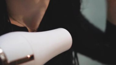 Uzun esmer saçlar, kuaförde saç kurutma makinesiyle kurutuluyor.