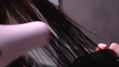 Uzun esmer saçlar, kuaförde saç kurutma makinesiyle kurutuluyor.