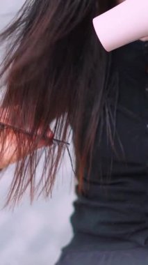 Uzun esmer saçlar, kuaförde saç kurutma makinesiyle kurutuluyor.