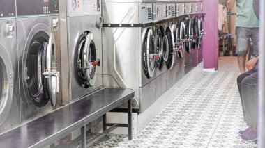 Aydınlık alanda sıralanmış çamaşır makineleri ve duvarlı iç döşemeleri olan şehir çamaşırhanesi..