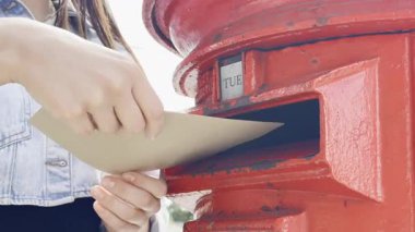 Şehir caddesinde mektupları klasik kırmızı posta kutusuna postalayan genç bir kadın.