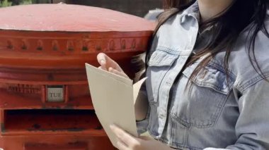 Şehir caddesinde mektupları klasik kırmızı posta kutusuna postalayan genç bir kadın.