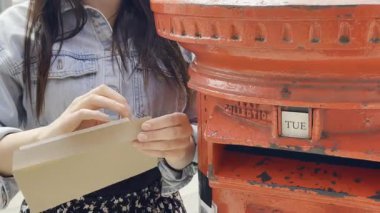 Şehir caddesinde mektupları klasik kırmızı posta kutusuna postalayan genç bir kadın.