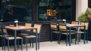 Boş güneşli terası olan rahat bir kafede basit açık masa ve sandalyeler.