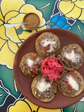 Traditional garnachas served on a clay plate at a restaurant in Oaxaca, Mexico. Deep-fried beef on masa with salsa and cheese. Top View. clipart