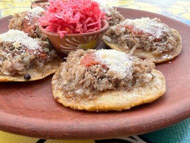 Traditional garnachas served on a clay plate at a restaurant in Oaxaca, Mexico. Deep-fried beef on masa with salsa and cheese. Close up from the side. clipart