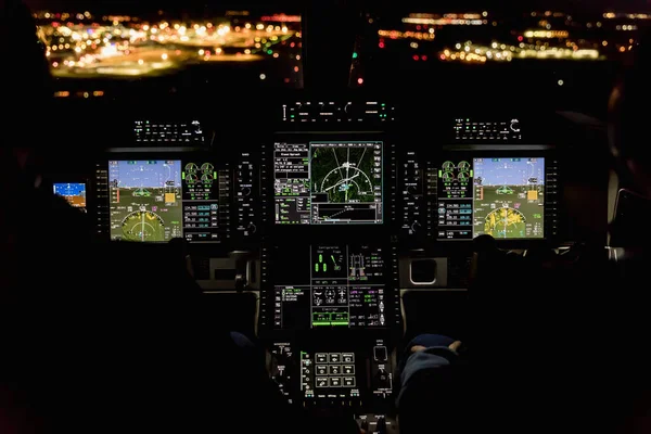 View from the cockpit of a modern airplane landing at an illuminated airport at night. Illuminated glass cockpit dashboard while landing at an airport at night.