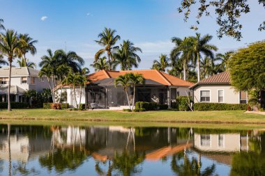 Güneşli bir günde Güney Florida 'da güzel bir yazlık. Florida 'nın güneybatısındaki bir gölün kıyısındaki tipik beton ev. Palmiye ağaçları, tropik bitkiler ve çiçekler, çimenler ve çam ağaçları. Florida.