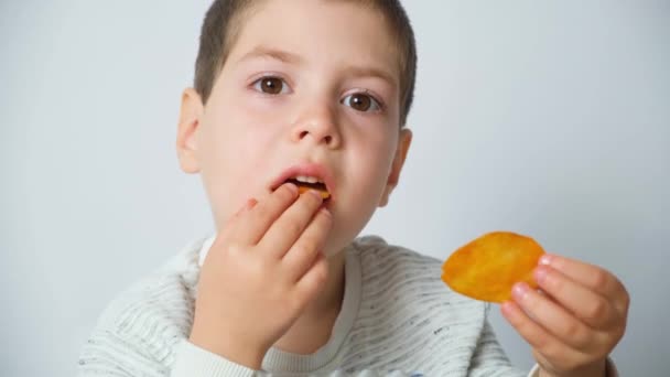 漂亮的学龄前男孩在白色背景下吃着美味的脆薯片 — 图库视频影像