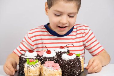 5 yaşındaki mutlu bir çocuk lezzetli bir pastaya bakar ve beyaz bir arka planda gülümser..