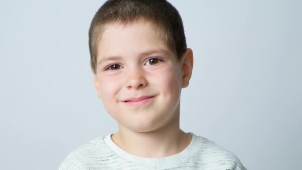 可愛い5歳の男の子が笑顔で まばたきをして 白い背景を見ています — ストック動画