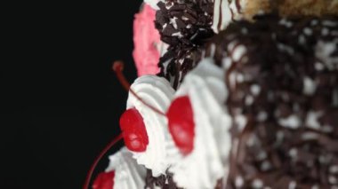 Çikolatalı, kirazlı ve kremalı kekler siyah arka planda dönüyorlar.