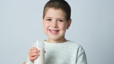 5 yaşında yakışıklı bir çocuk beyaz arka planda mayalanmış bir bardak sütü elinde tutuyor..