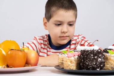 5 yaşındaki tatlı çocuk meyve ve keklerin önünde oturur ve ne yiyeceğini seçer..