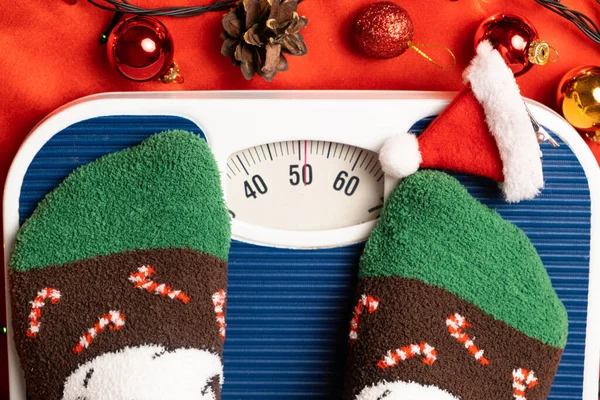 stock image A woman in Christmas socks stands on the scales, weighs herself after gluttony during the holidays.